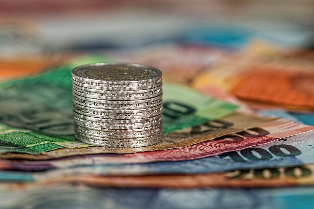 services-03 A stack of coins on top of various colored banknotes, symbolizing finance and currency.